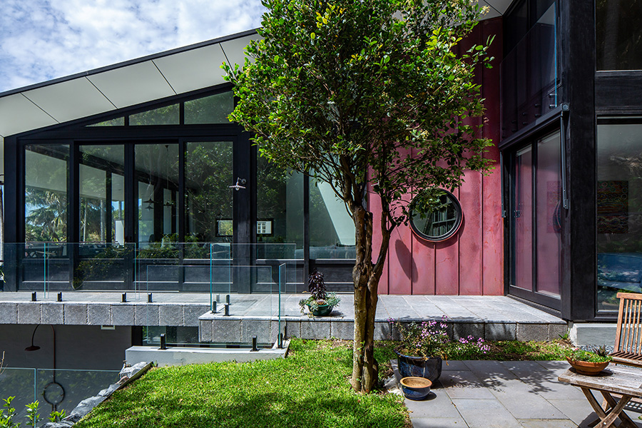 External view of house with black windows, a round custom made double glazed bushfire safe window and lift slide sliding doors
